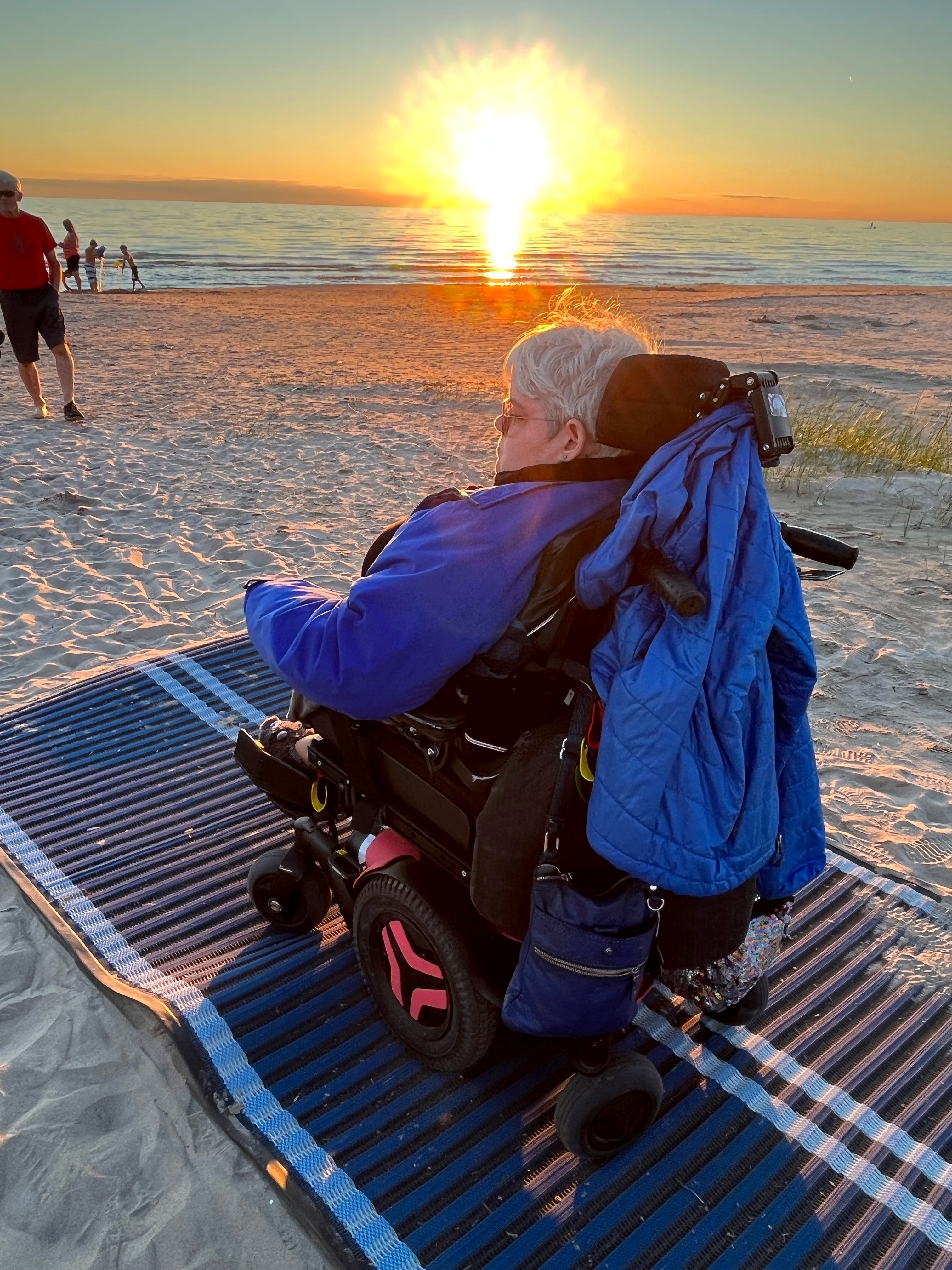Person watching a sunset in a wheelchair on a mobi mat